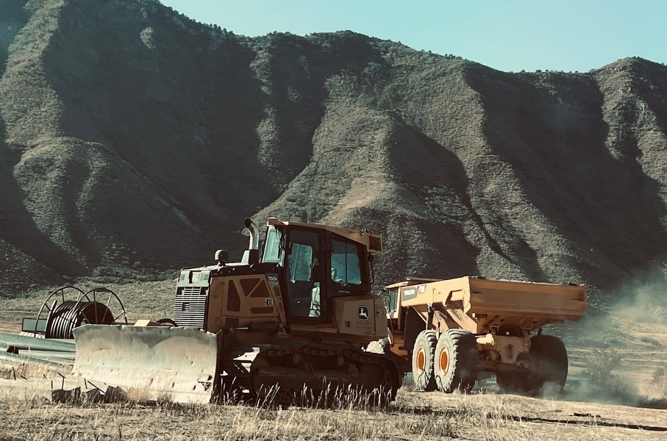 Bulldog Construction heavy equipment — dozer and dump truck working on a site with Colorado mountains in the background.